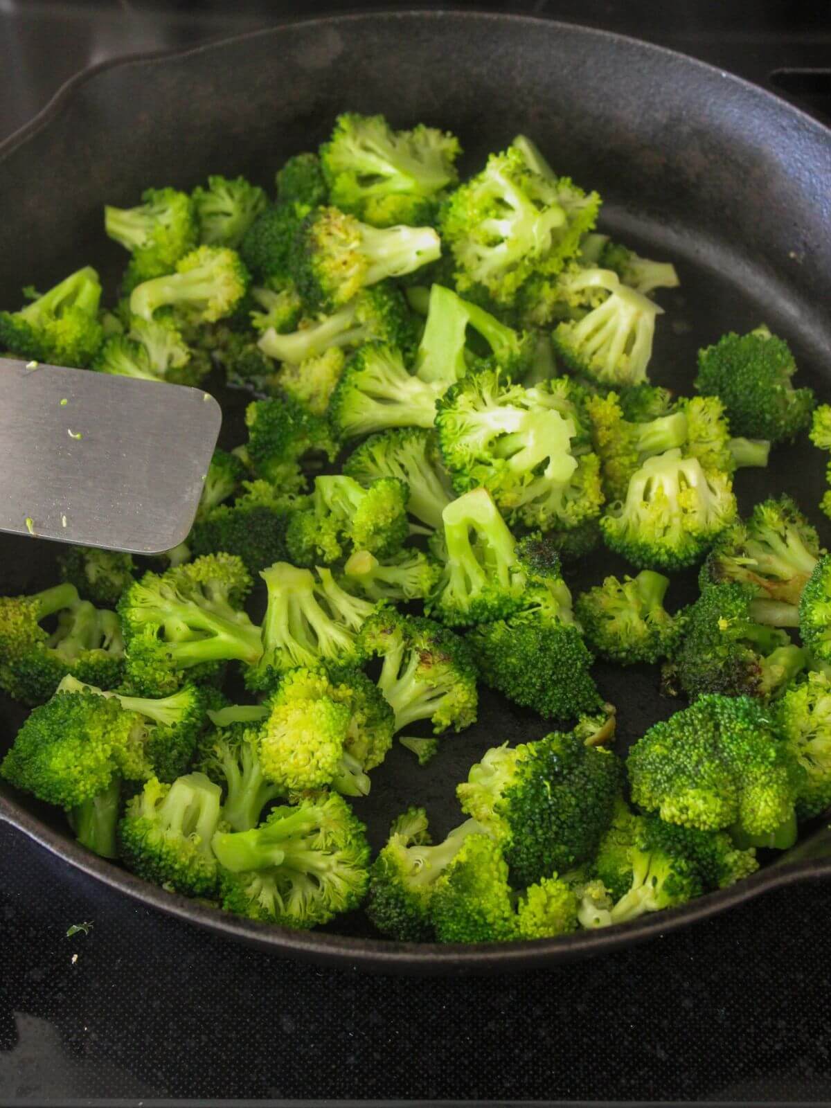 broccoli cooking in a cast-iron pan with a stainless steel spatula