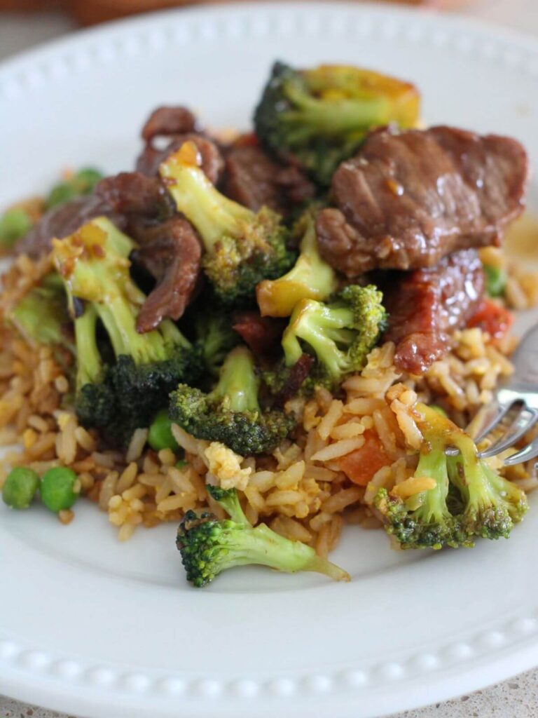 Beef and Broccoli Plated on a white plate over fried rice with a silver spoon 