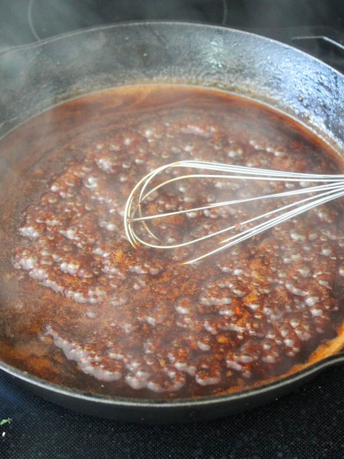 sauce bubbling and thickening in a cast-iron pan with a stainless steel whisk