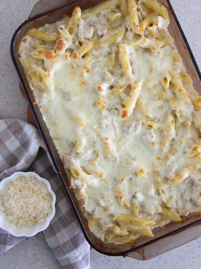 chicken alfredo pasta baked in glass dish ready to eat with a plaid napkin and a small dish of parmesan