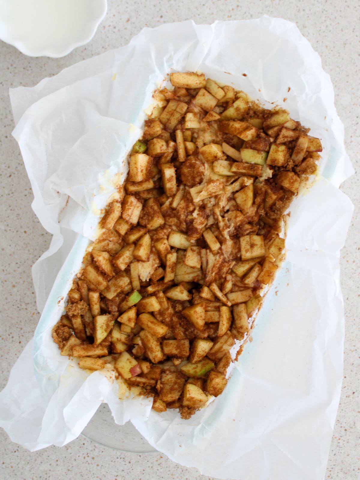 The apple fritter bread in a parchment lined loaf pan ready to bake