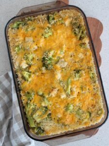 Cheesy Chicken Broccoli Casserole full view in a brown glass baking dish on a cutting board with a plaid napkin