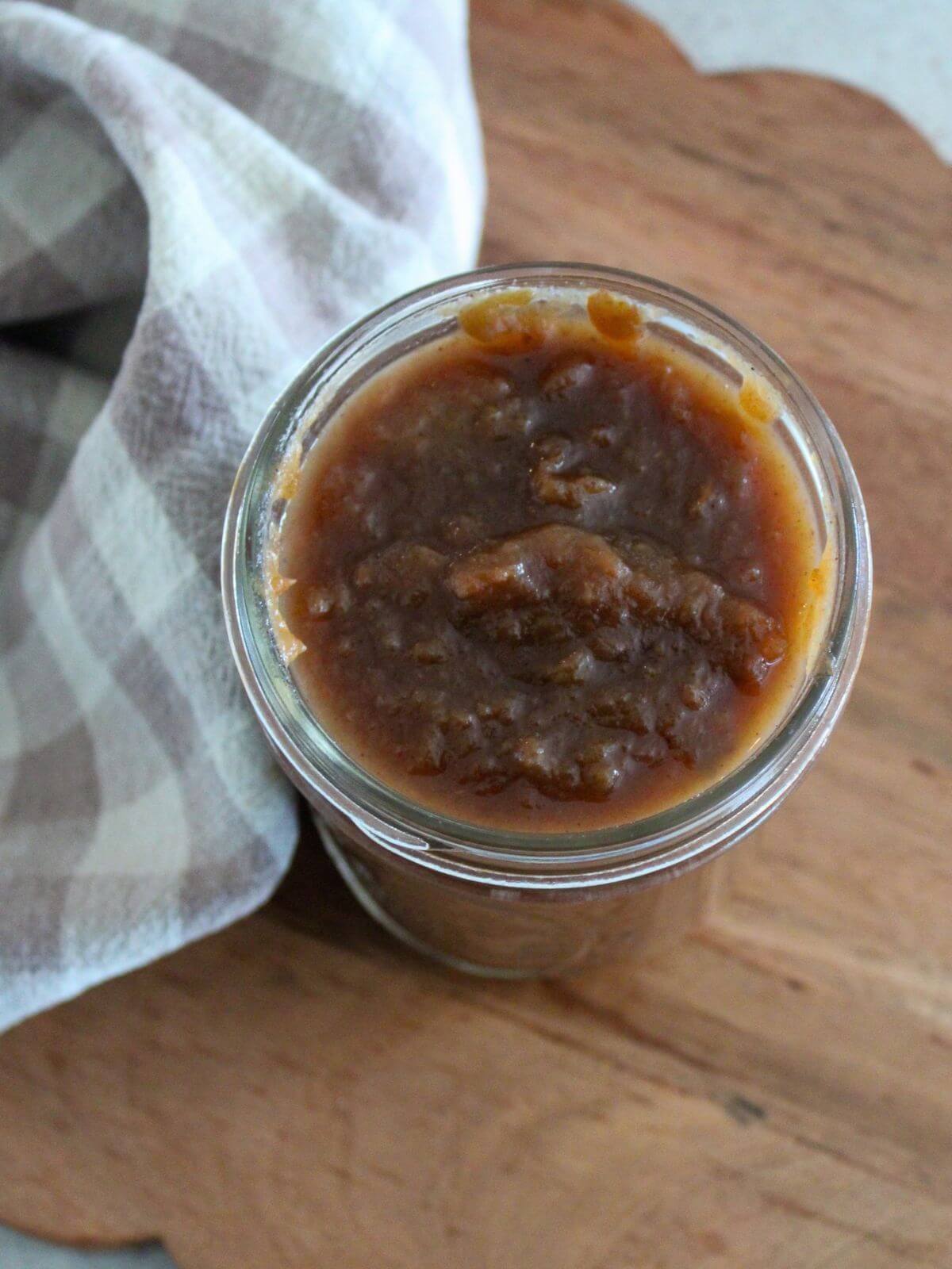 the apple butter transferred to glass jar on a wooden cutting board with a plaid napkin