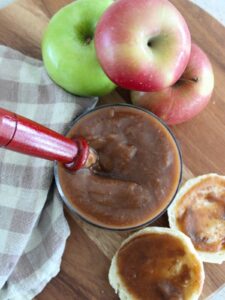 Slow Cooker Apple Butter in a glass jar with apples, apple butter on a biscuit and a plaid napkin around it all on top of a cutting board