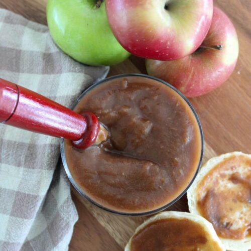 Slow Cooker Apple Butter in a glass jar with apples, apple butter on a biscuit and a plaid napkin around it all on top of a cutting board