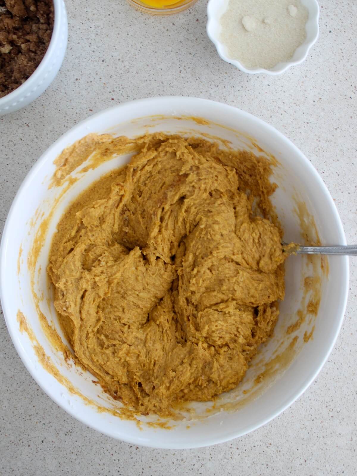 mixing the pumpkin batter in a white bowl with a silver spoon