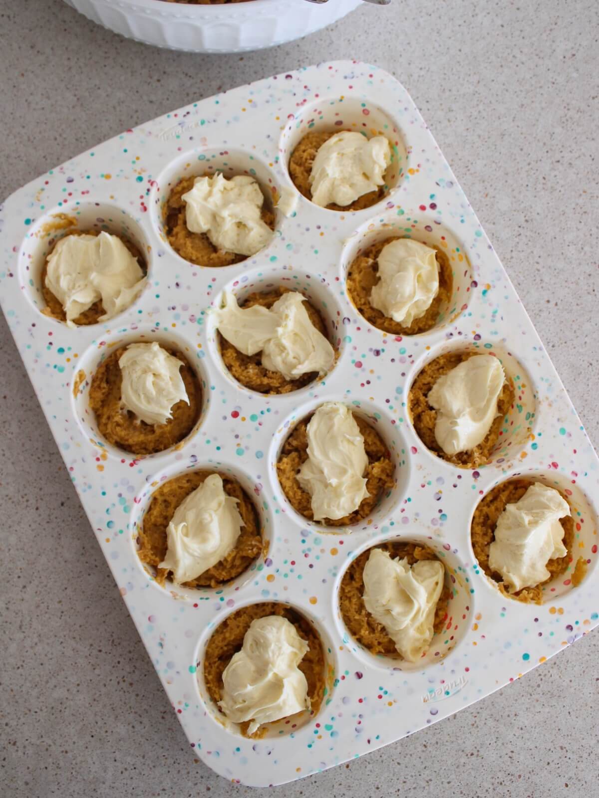 topping the pumpkin batter with cream cheese filling in the muffin pan