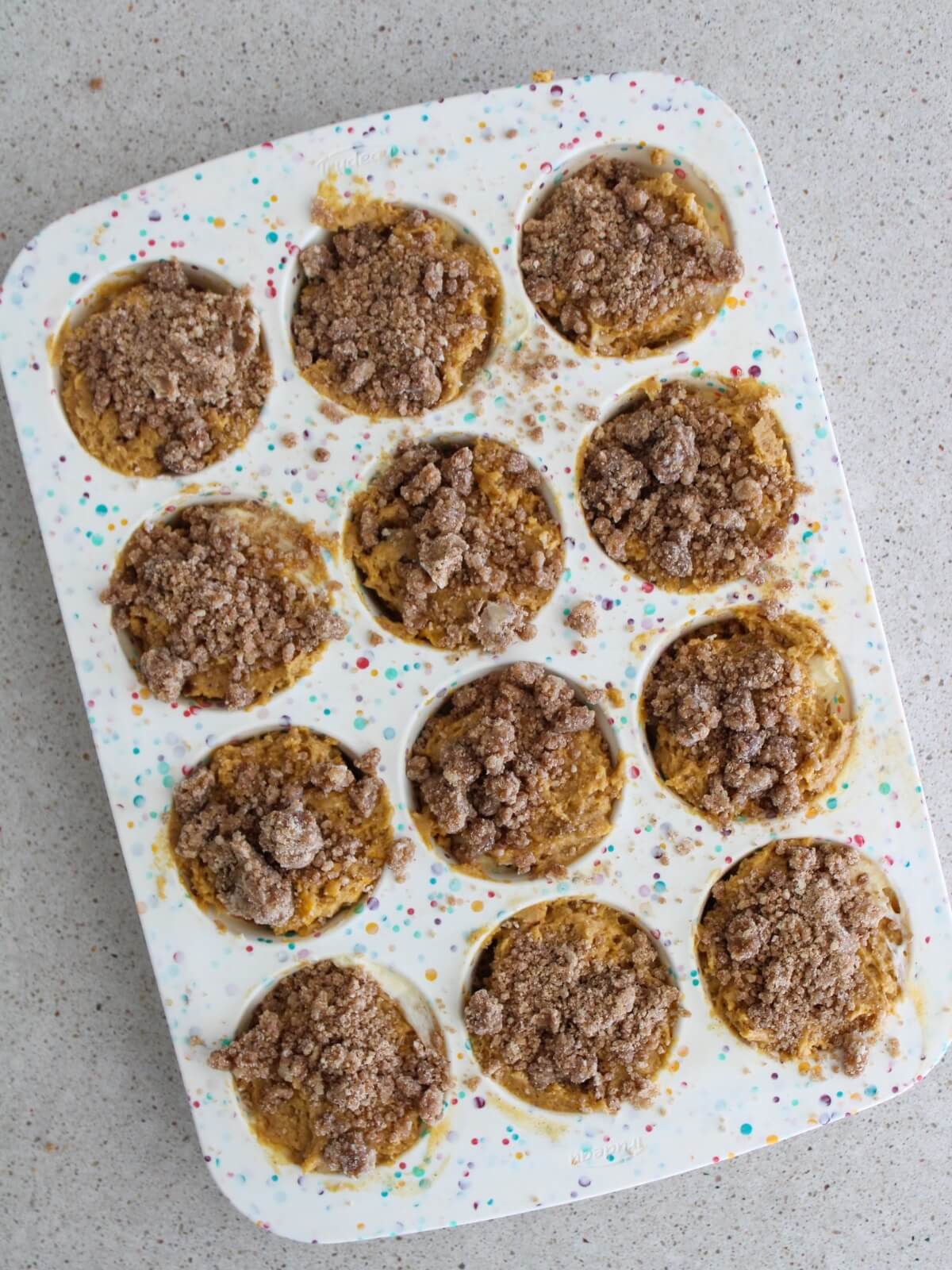 adding the crumble topping to the top of the muffins in the muffin pan