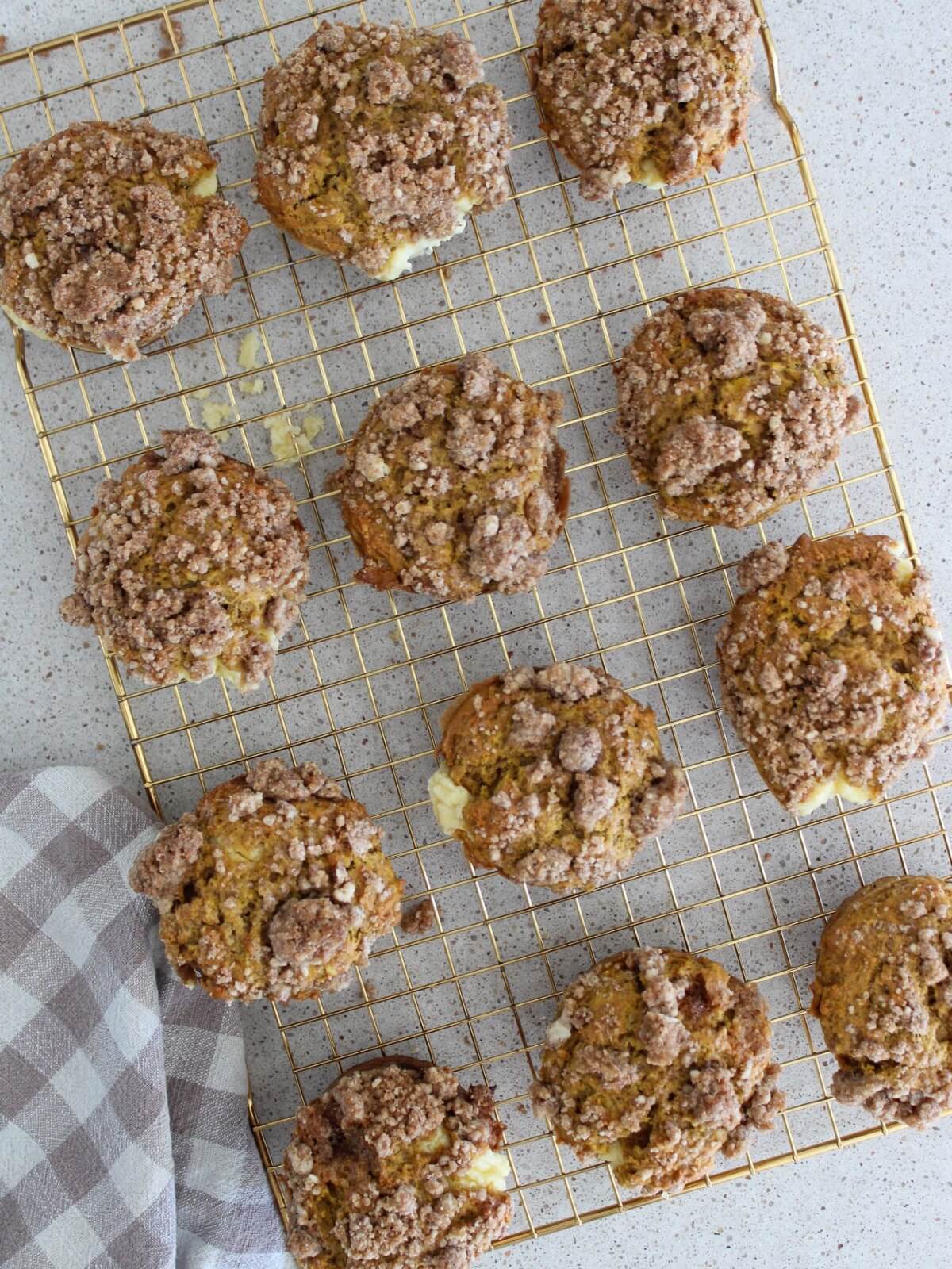 the pumpkin cream cheese muffins cooling on a gold cooling rack with a plaid napkin